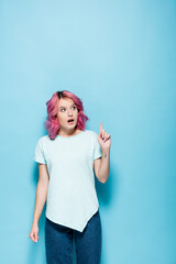 surprised young woman with pink hair pointing up on blue background