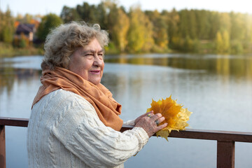 Portrait of a happy old woman in the autumn park near the river.