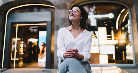 Cheerful hipster girl in classic spectacles for provide eyes correction and electronic headphones...