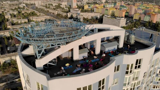 Aerial Shot Group of adults peoples doing yoga outdoors on the roof of the High Building. Outdoor group yoga classes back view. Many people do yoga exercises. Meditation and wellness lifestyle concept