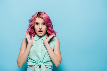 Obraz na płótnie Canvas surprised young woman with pink hair and open mouth on blue background