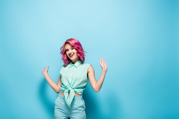 young woman with pink hair gesturing on blue background