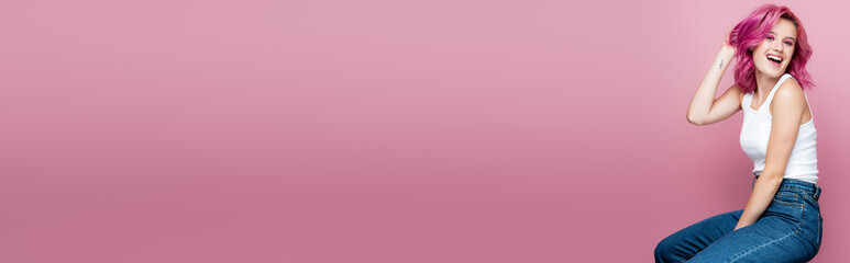 young woman with colorful hair and tattoo smiling isolated on pink, panoramic shot