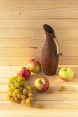 Still life with grapes, apples and a jug on a light wooden background. Vintage vintage ceramic wine jug. Rustic autumn still life. Vitamin complex. Healthy diet. The warm sunlight.
