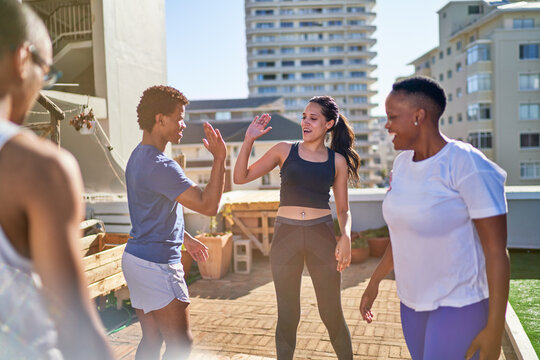 Young friends exercising and high fiving on sunny urban rooftop