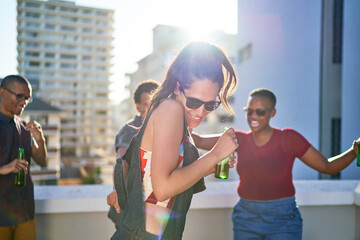 Happy young friends dancing and drinking beer on sunny urban rooftop