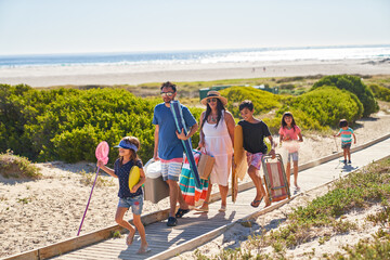 Family carrying chairs and toys on sunny beach boardwalk