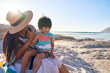 Mother applying sunscreen to nose of cute son on sunny beach