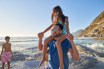 Happy father carrying daughter on shoulders on sunny ocean beach