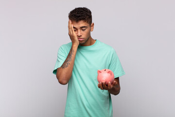 young man with a piggy bank feeling bored, frustrated and sleepy after a tiresome, dull and tedious...