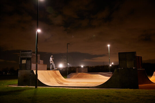 Young man skateboarding on skate park ramp at night
