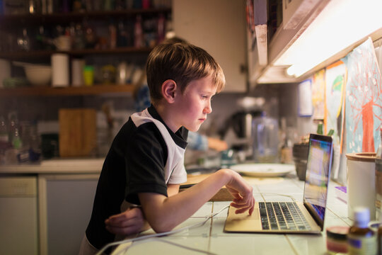 Boy doing homework at laptop on kitchen counter