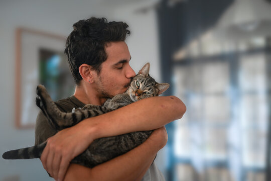 hombre joven sostiene a un gato entre sus brazos y lo besa