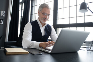 Concentrated at work. Mature man in full suit using laptop while working in modern office