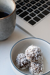 Focus on cup of black coffee and a plate with homemade raw chocolate balls, which is a classic no bake pastry in Sweden and Denmark, with laptop keyboard in the background