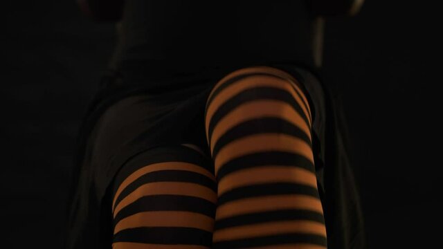 Unrecognizable woman wearing in striped black and orange color stockings sitting in chair with crossed legs, open them and cross again.