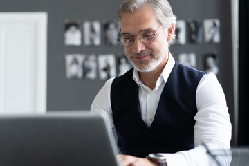 Concentrated at work. Happy mature man in full suit using laptop while working in modern office