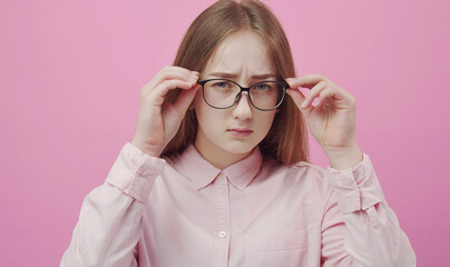 Young lady touching glasses with both hands looking at camera with doubt or distrust, studio shot