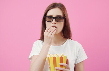 Front view of impassive female model in glasses eating popcorn looking at camera isolated on pink