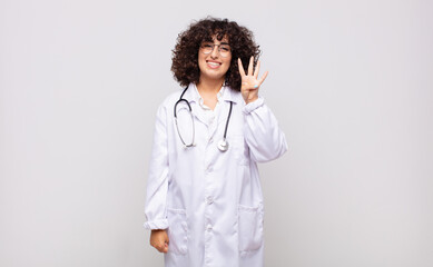 young woman physician smiling and looking friendly, showing number four or fourth with hand...