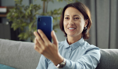 Portrait of a adult brunette taking selfie or talking by video call using smartphone staying home