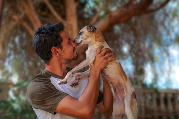 Perro marrón lame la  nariz de un joven en un jardín.