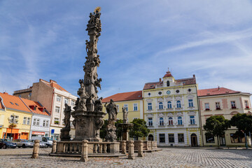 Fototapeta na wymiar Holy Trinity Column, fountain with a statue of St. Florian and historical buildings in the main Republic square of Duchcov in sunny day, Northern Bohemia, Czech Republic