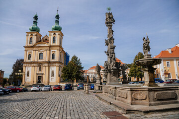 Church of the Annunciation, Holy Trinity Column and fountain with a statue of St. Florian in the main Republic square of Duchcov in sunny day, Northern Bohemia, Czech Republic