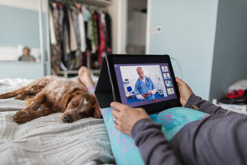 Woman with digital tablet video chatting with doctor on bed with dog