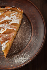 A piece of homemade pie on a plate of powdered sugar in a rustic style. Sliced apple pie with icing close-up and copy space.