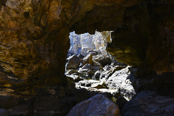 Exit from a stone cave on the Mediterranean coast. Dungeon. Shallow water. Bright sunlight. Stones in the water.