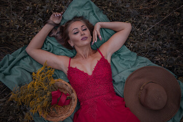 attractive woman with yellow wildflowers in red dress lies on the grass