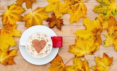 cup of coffee with a heart of cinnamon and gift box on the table, maple leaves around