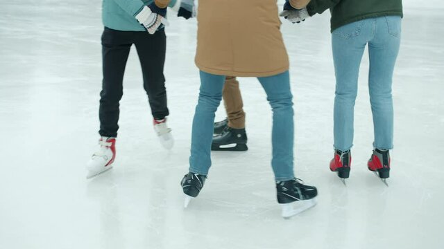 Low shot of people's legs men and women ice-skating in park together wearing skates and warm clothes. Healthy lifestyle and winter sports concept.