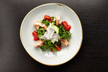 Salad with shrimps, tomatoes and arugula, on a white plate, on a dark background