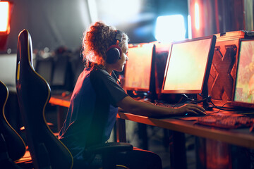 Cybersport concept. Side view of a focused teenage girl, professional gamer wearing headphones participating in eSport tournament - obrazy, fototapety, plakaty
