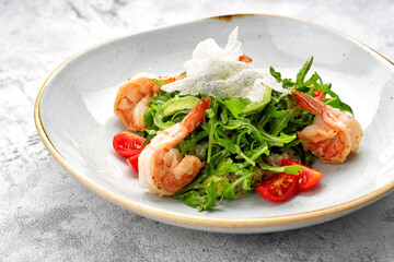 Salad with shrimps, tomatoes and arugula, on a white plate, on a light background