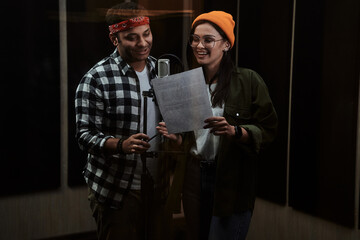 Portrait of young man and woman, duet looking at lyrics, singing into a condenser microphone while...