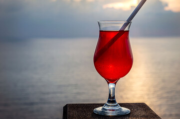 Colorful alcoholic exotic cocktail in a glass isolated against the background of the Mediterranean Sea in the rays of sunset sun. Big plan. Romantic background with the ability to insert text.