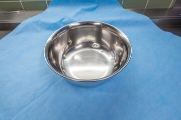 large silver saline bowl is wrapped in a blue paper towel in an operating room