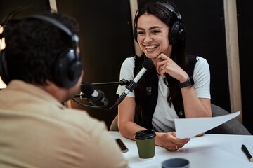Portait of happy female radio host smiling, listening to male guest, presenter and holding a script...