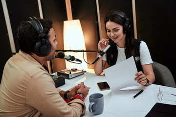Portait of happy female radio host smiling, talking to male guest, presenter while moderating a...