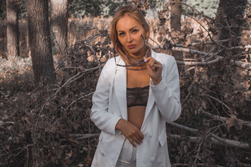 fashionable attractive woman in a white suit and sunglasses on a background of white trees in the...