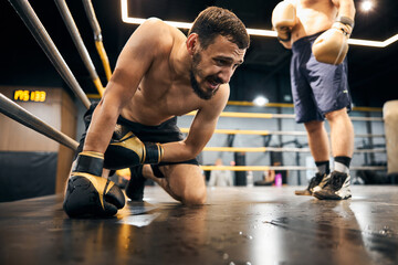 Fototapeta na wymiar Hopeless male boxer is kneeling in the ring