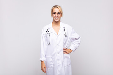 young woman physician smiling happily with a hand on hip and confident, positive, proud and friendly attitude