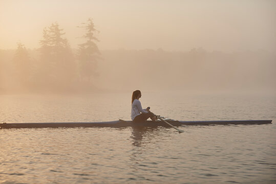 Side view of woman rowing single scull in lake at early morning