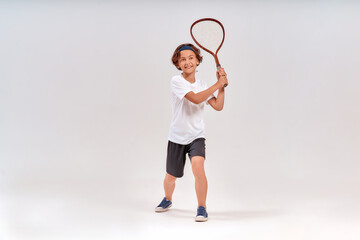 Tennis is fun. Full-length shot of a happy teenage boy holding tennis racket and smiling isolated over grey background