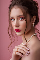 Beautiful woman wearing elegant natural river white pearl necklace, earrings, posing on pink...