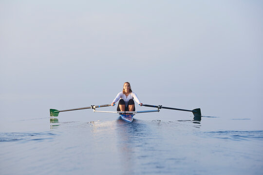 Middle aged woman rowing on lake at early morning with mist over water.