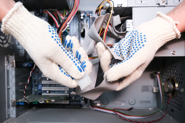 A technician in gloves holding cables of a broken computer in order to find a breakdown